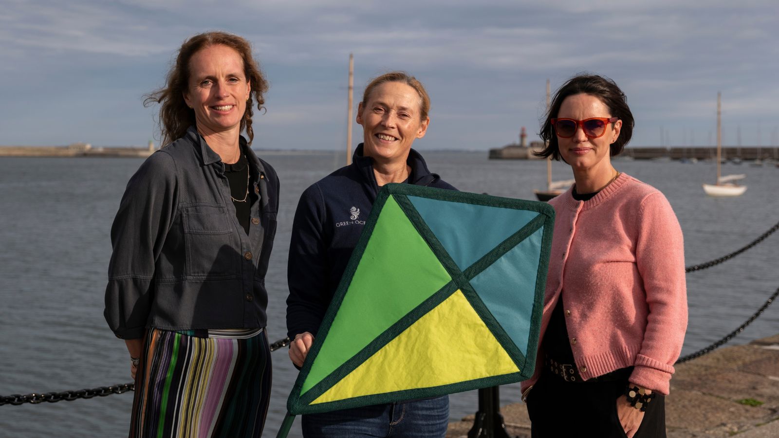 Three women smiling in front of the sea one holding a kite.