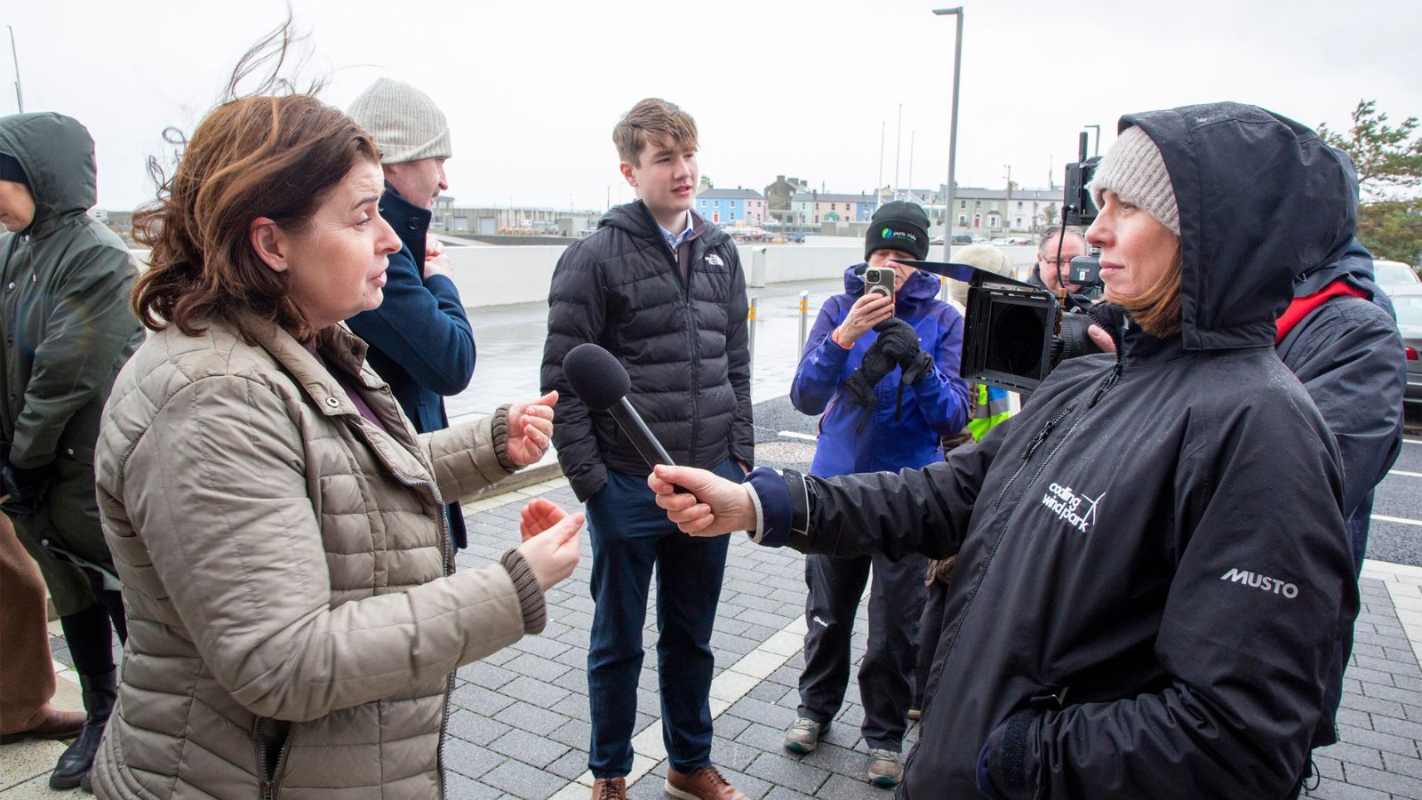 Group of people outside in the rain. One woman interviewing another with a microphone